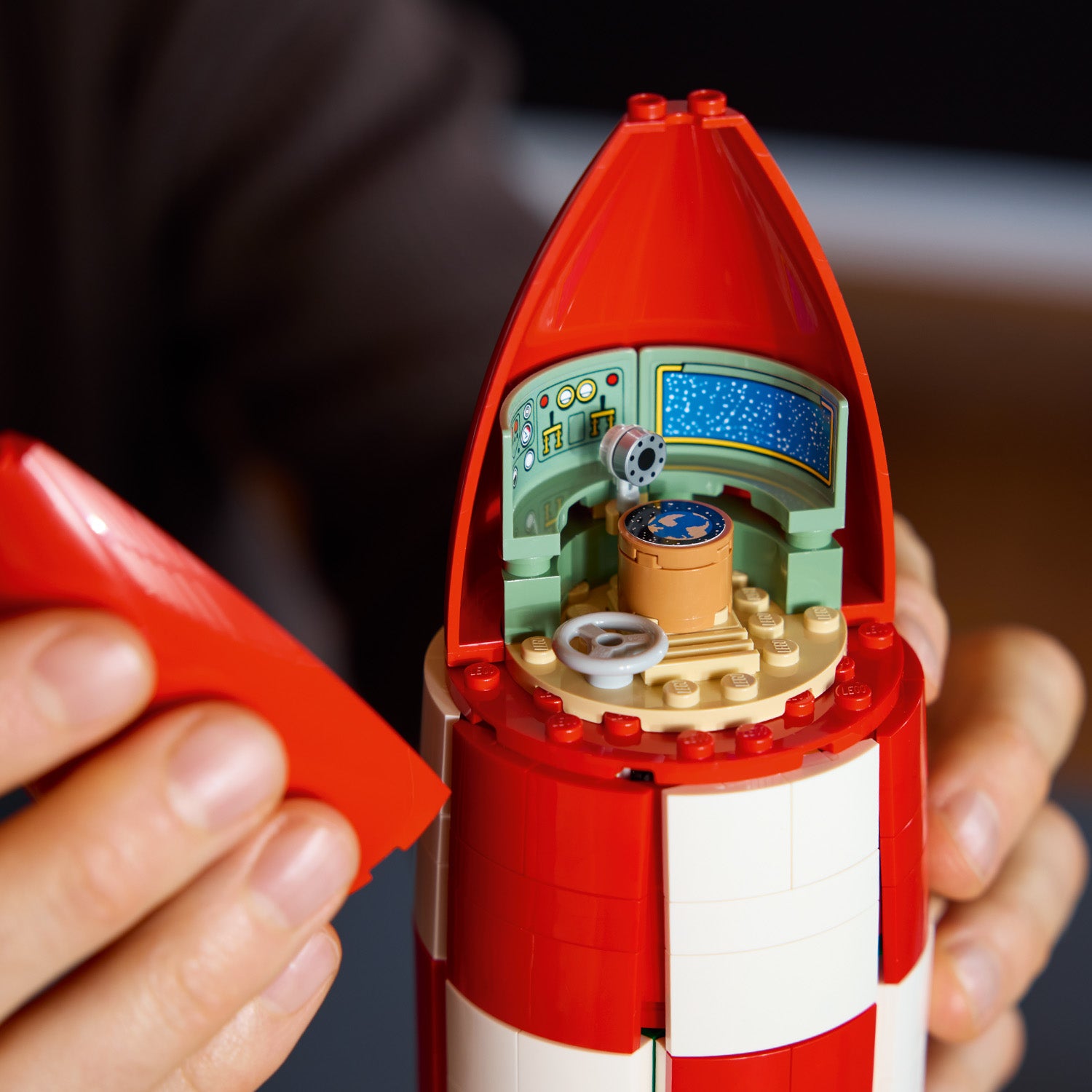 Close-up of a red and white toy rocket with a detailed interior held by hands.