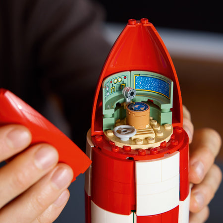 Close-up of a red and white toy rocket with a detailed interior held by hands.