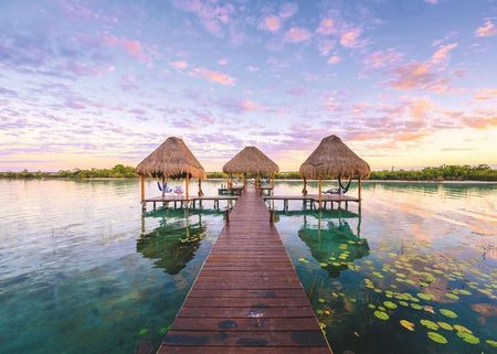 ravensburger jigsaw puzzle image of Wooden dock leading to three thatched-roof structures over water with a colorful sky.