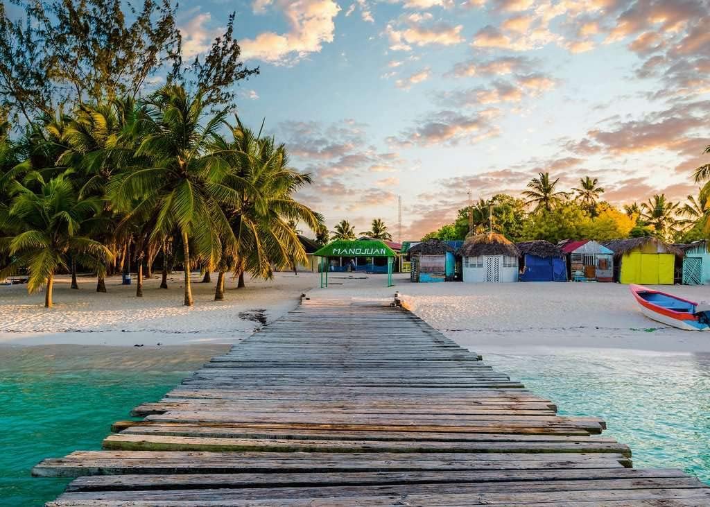 ravensburger jigsaw puzzle image of Wooden dock leading to a tropical beach with palm trees and colorful huts.