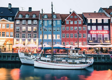 ravensburger jigsaw puzzle image Colorful buildings along a waterfront with boats docked in front, illuminated by evening lights.