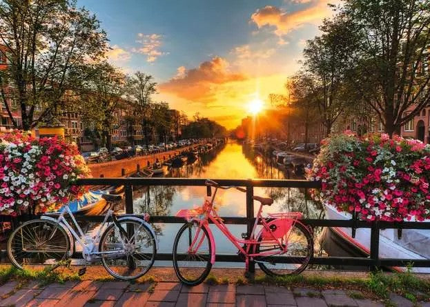 1000-piece Ravensburger jigsaw puzzle "bicycles in Amsterdam" featuring a scenic canal with bicycles and flowers at sunset.