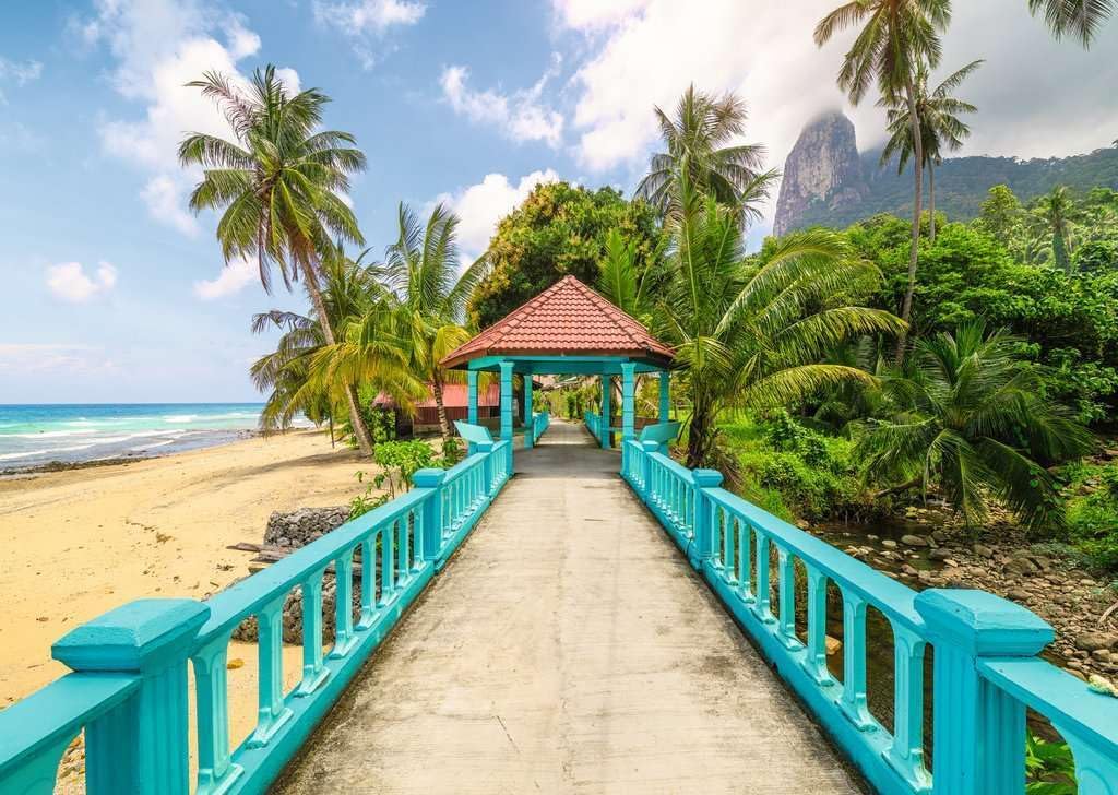 ravensburger colorful bridge in malaysia jigsaw puzzle of Beachside pathway with turquoise railings leading to a wooden hut, surrounded by palm trees and ocean.