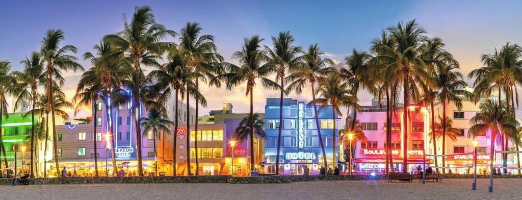 ravensburger night glow on ocean drive panoramic jigsaw puzzle of Colorful building facades with palm trees on a beach at dusk.