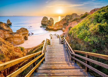ravensburger stairway to camilo beach, algarve jigsaw puzzle featuring Wooden staircase leading to a beach with rock formations and a sunset.